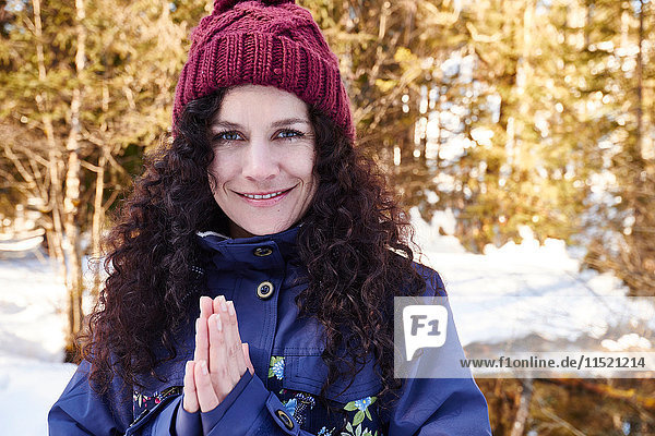 Porträt einer Frau  die Yoga praktiziert  mit den Händen zusammen im verschneiten Wald  Österreich