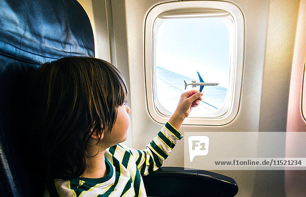 Junge spielt mit Spielzeugflugzeug am Flugzeugfenster