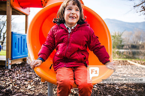Junge sitzt auf orangefarbener Spielplatzrutsche