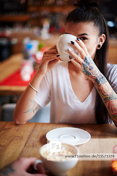 Tätowierte Frau in Café  die Kaffee trinkt und in die Kamera schaut