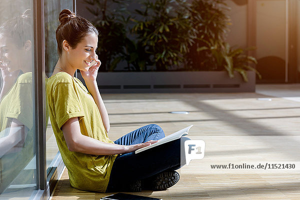 Junge Studentin sitzt im Schneidersitz im Freien und unterhält sich mit einem Smartphone