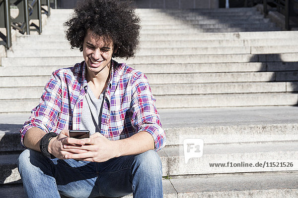 Portrait of smiling young man sitting on stairs looking at cell phone