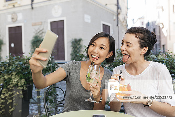 Italy  Padua  two young women pulling funny faces while taking selfie at sidewalk cafe