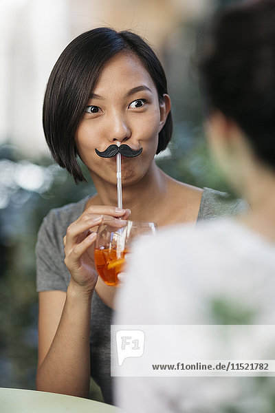Porträt einer jungen Frau mit Schnurrbart und Cocktail im Straßencafé mit ihrer Freundin