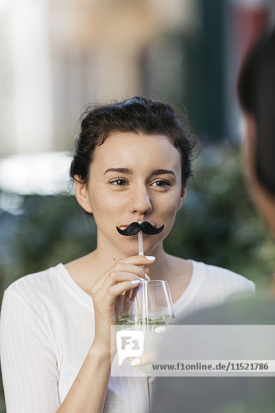 Porträt einer jungen Frau mit Schnurrbart und Cocktail im Straßencafé mit ihrer Freundin