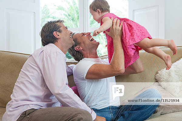Mature male couple playing with baby daughter on sofa