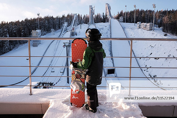 Rückansicht eines Jungen mit Snowboard oben auf der Skipiste