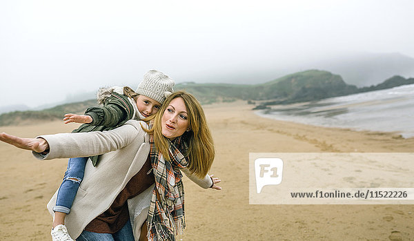 Happy woman and daughter pretending to fly on the beach in winter