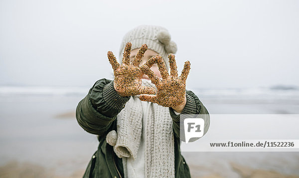 Mädchen zeigt ihre sandigen Hände am Strand im Winter