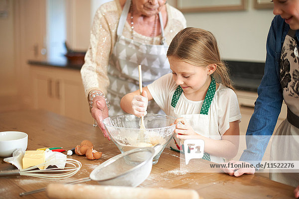 Ältere Frau und Enkelinnen rühren Keksmischung in Schüssel
