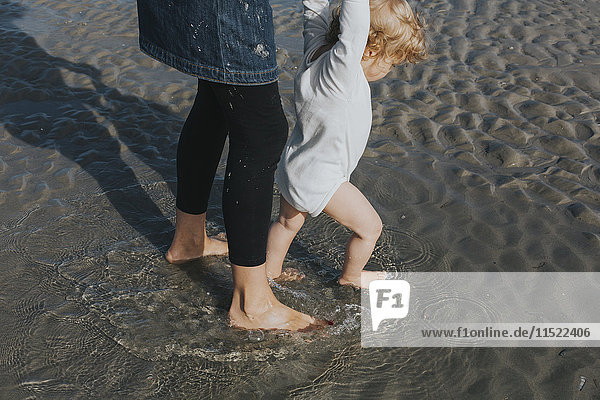Mother with little daughter wading in water on the beach