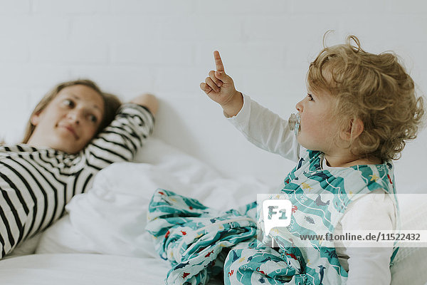 Kleines Mädchen mit Mutter im Bett  die mit dem Finger auf sie zeigt.
