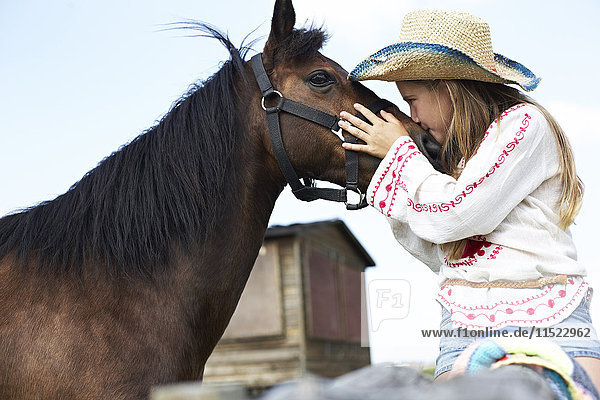 Mädchen mit Strohhut küssendes Pferd