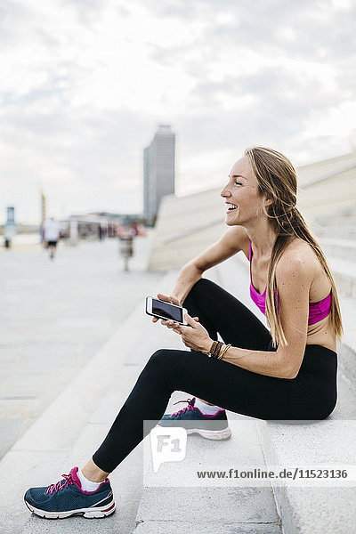 Young woman sitting on stairs after training  using smart phone