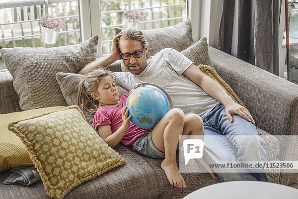 Father and daughter lying with globe on sofa