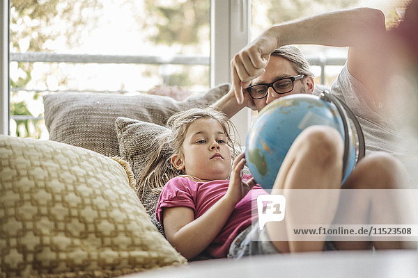 Vater und Tochter liegen mit Globus auf Sofa