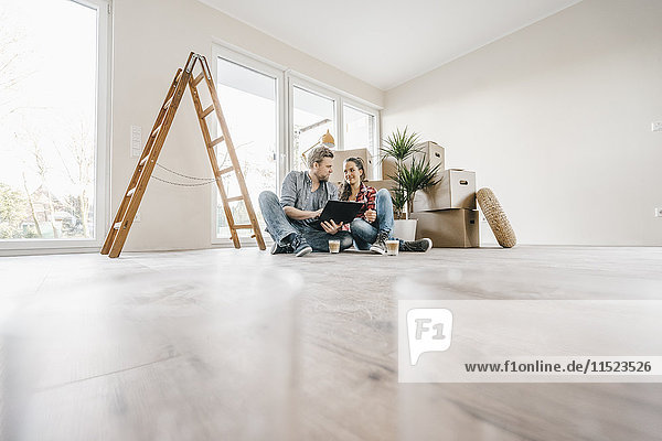 Pärchen sitzen auf dem Boden ihres neuen Zuhauses inmitten von Umzugskartons.