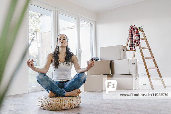 Frau sitzend auf Kissen in ihrer neuen Wohnung  meditierend