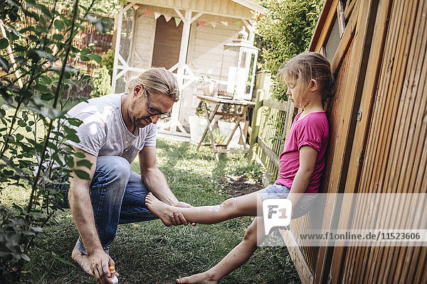 Father applying sunscreen on daughter's legs in garden