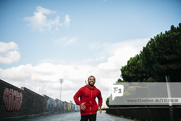 Smiling young man wearing red hoodie running in the city