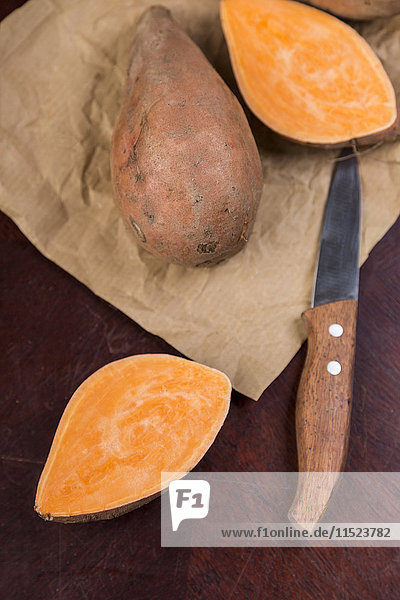 Sliced and whole sweet potatoes and kitchen knife on brown paper