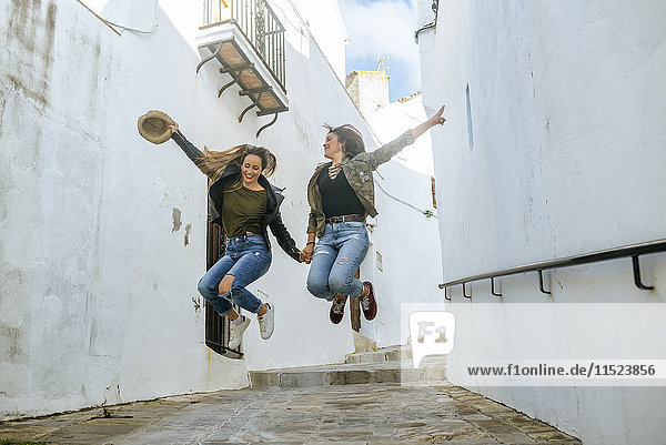 Zwei glückliche junge Frauen  die in einer Gasse einer Stadt springen.