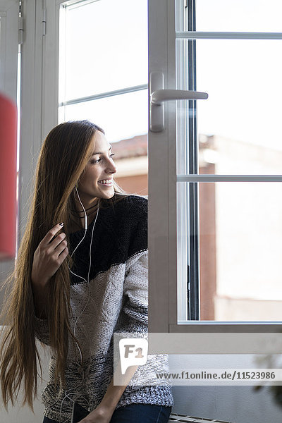 Lächelnde junge Frau mit Kopfhörern  die aus dem Fenster schauen.