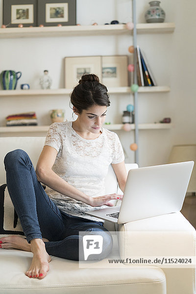 Woman sitting on couch at home using laptop