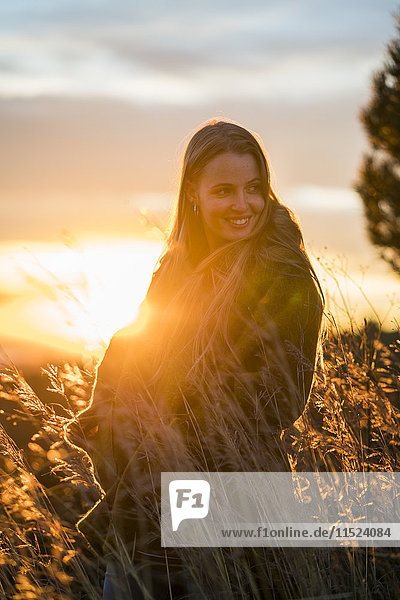 Lächelnde junge Frau in der Natur bei Sonnenuntergang  die sich umdreht
