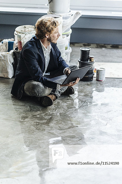 Businessman sitting on floor with laptop and paint buckets