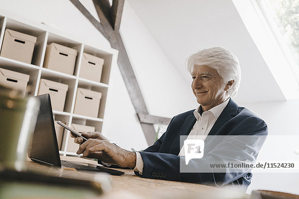 Lächelnder Senior-Geschäftsmann mit Laptop in seinem Büro