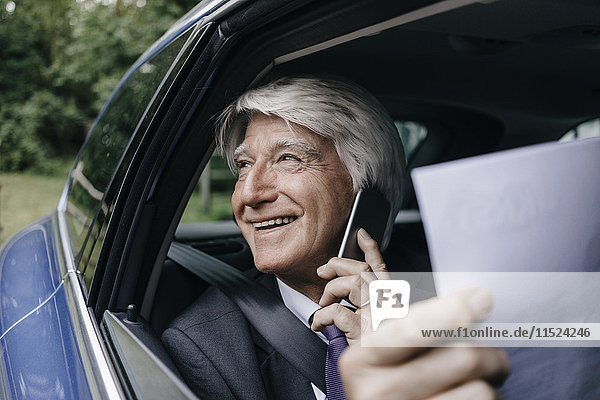 Lächelnder Geschäftsmann mit Dokumenten am Telefon im Auto