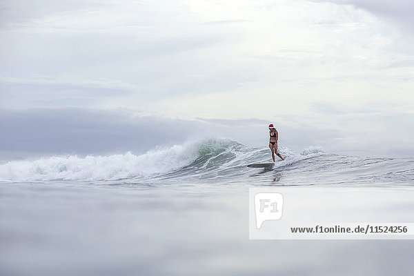 Indonesien  Bali  Frau mit Nikolausmütze surft auf einer Welle