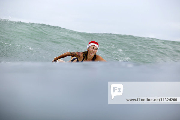 Indonesien  Bali  lächelnde Frau auf dem Surfbrett mit Weihnachtsmütze