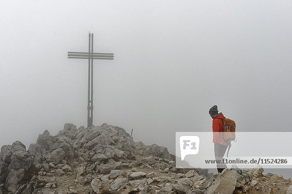 Italien  Südtirol  Mann am Gipfelkreuz des Weisshorns bei starkem Nebel