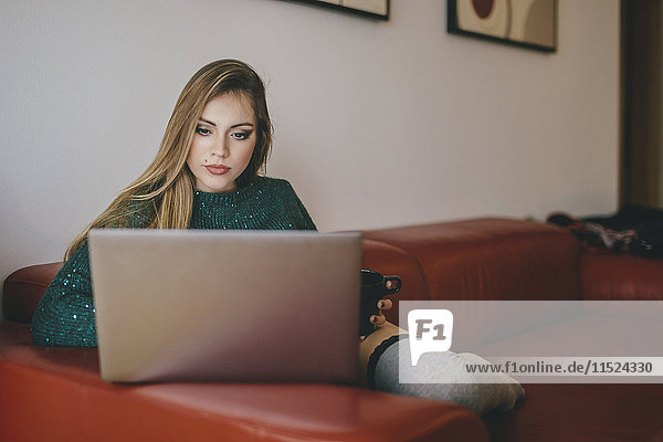 Junge Frau auf der Couch sitzend mit einer Tasse Kaffee am Laptop