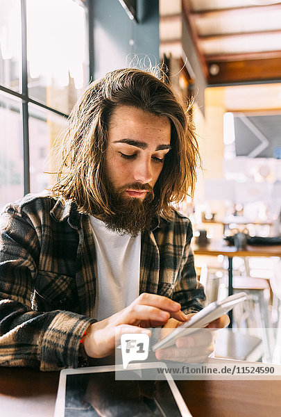Stilvoller junger Mann mit Handy im Cafe