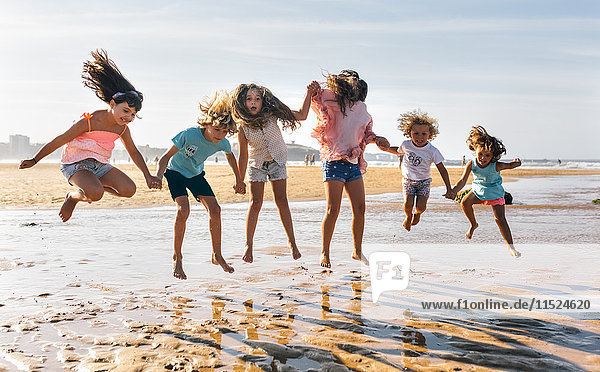 Group of six children jumping in the air on the beach