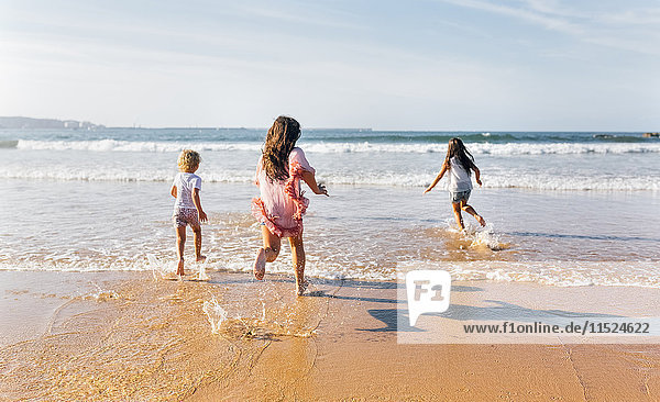 Back view of three children running into the sea