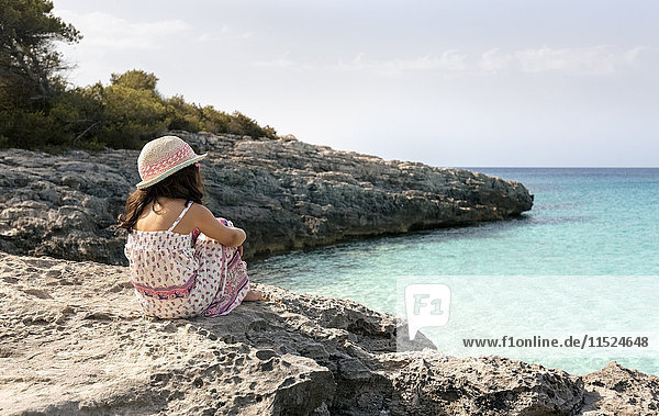 Mädchen am Strand sitzend mit Blick aufs Meer