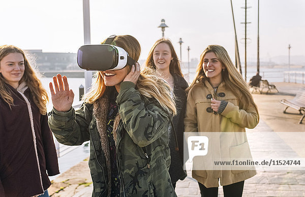 Teenager-Mädchen,  das eine VR-Brille trägt,  während ihre Freunde sie beobachten.