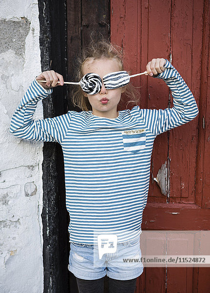 Mädchen,  das die Augen bedeckt mit Lakritz-Lolly-Pops