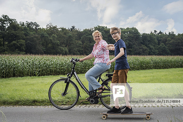 Enkel und Großmutter fahren gemeinsam Fahrrad und Skateboard