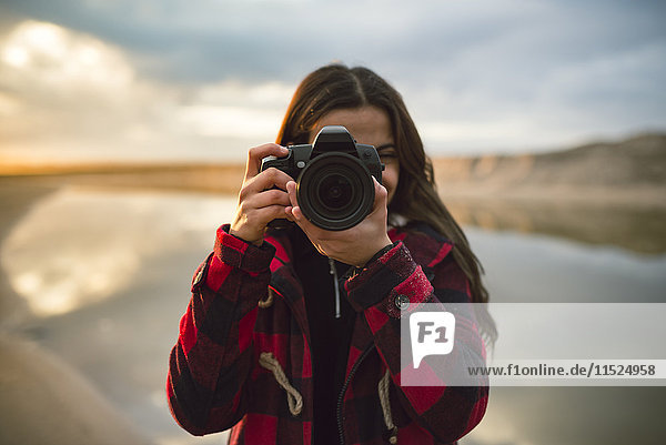 Junge Frau fotografiert mit Kamera am Strand