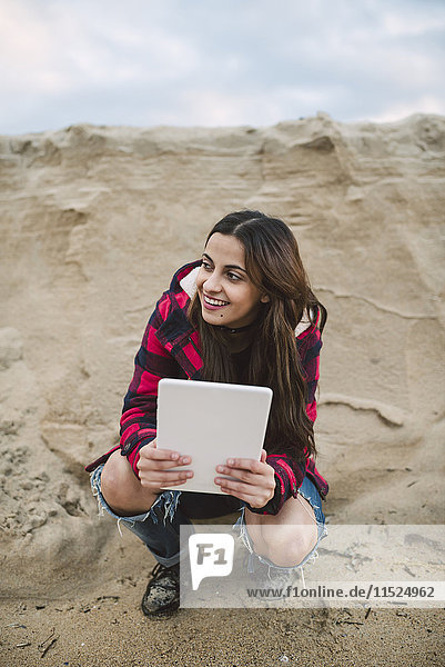 Young woman with tablet crouching on the beach