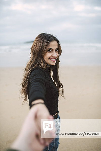 Porträt einer glücklichen jungen Frau  die am Strand die Hand hält
