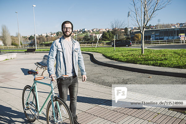 Junger Mann  der mit seinem Fixie Bike in einem Park spazieren geht.