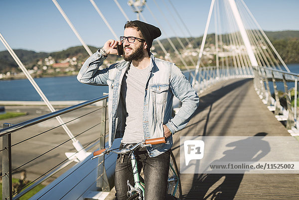 Junger Mann mit Fixie Bike auf einer Brücke am Telefon