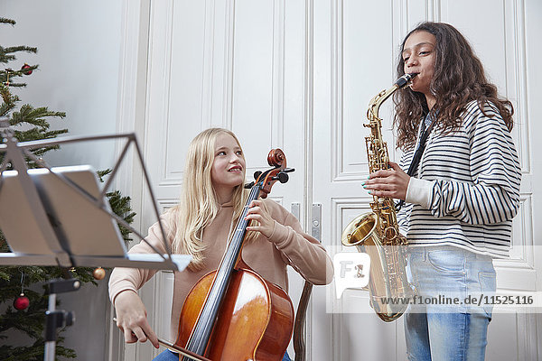 Two girls playing cello and saxophone at Christmas tree