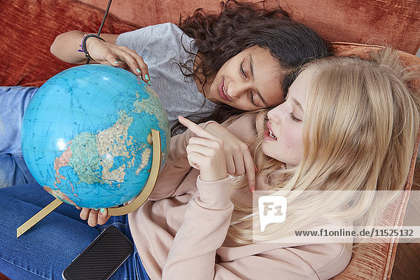 Zwei Mädchen liegen auf der Couch und zeigen auf den Globus.
